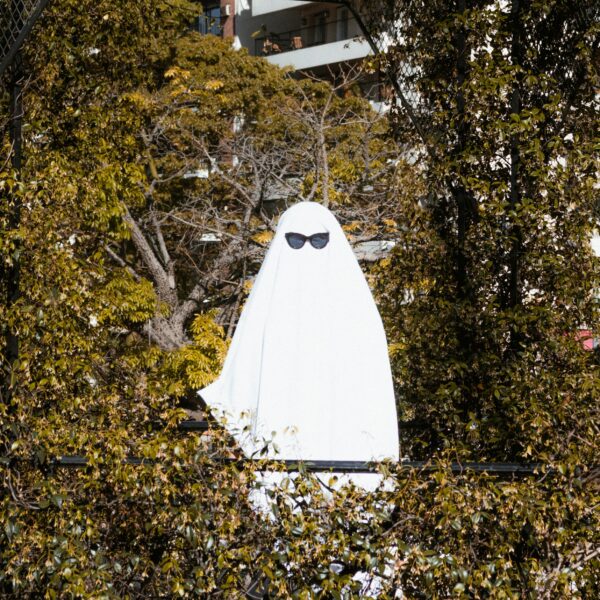 A person in a ghost costume with sunglasses hidden among trees in a Buenos Aires park.