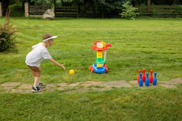 Boy playing with toy bowling set on grass, showing active outdoor fun.