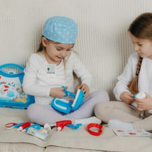 Two girls playing dentist with a toy kit indoors, showing creativity and fun.