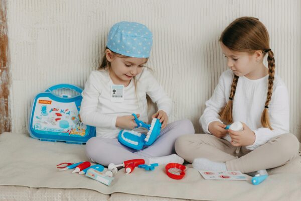 Two girls playing dentist with a toy kit indoors, showing creativity and fun.