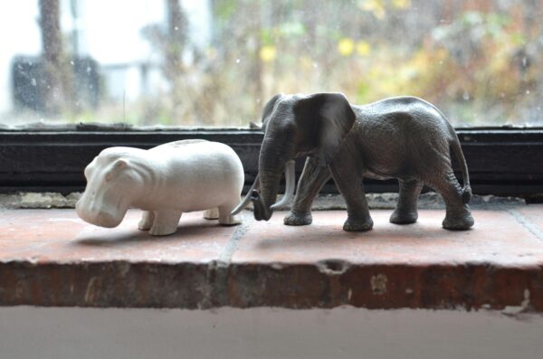 Artistic elephant and hippopotamus figurines on a brick windowsill indoors, showcasing decorative charm.