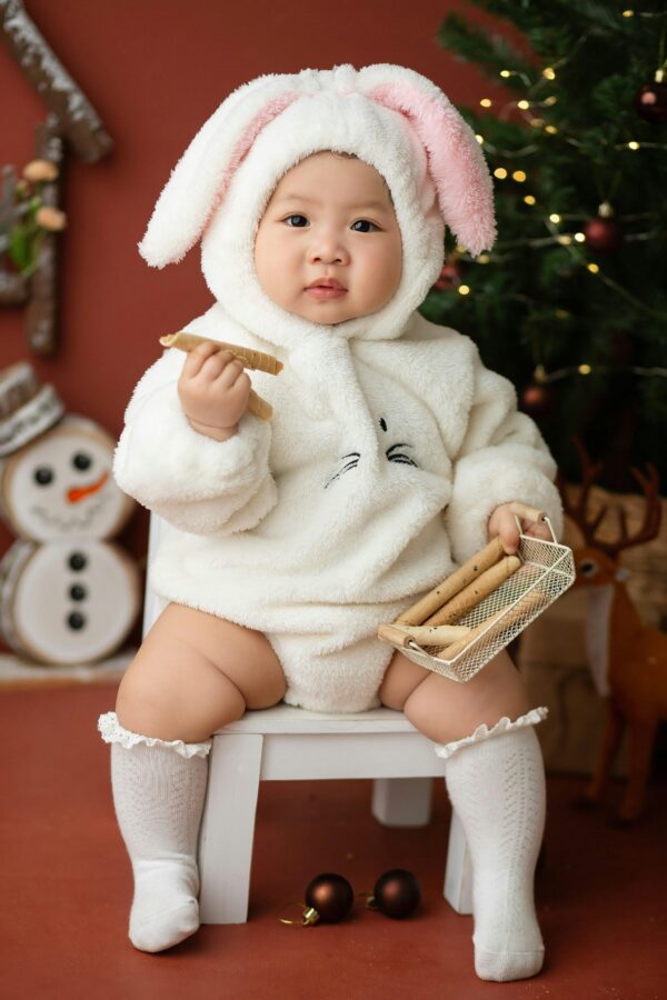 Cute baby in bunny costume with festive Christmas decorations, playing indoors.