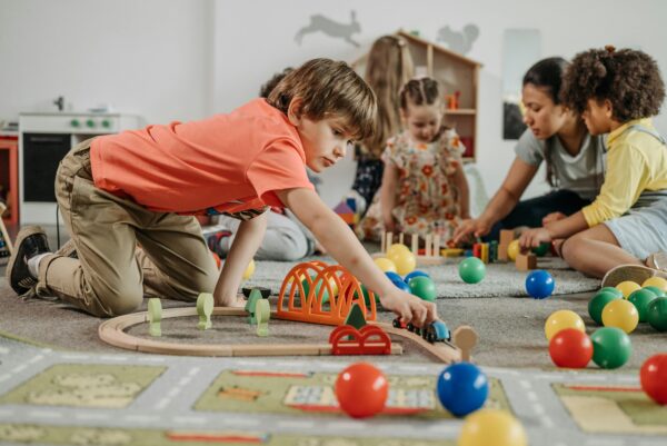 Children engaged in play with toys and an educator in a kindergarten setting.